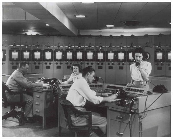 Oak Ridge Control Room K-25 Two men work at desks while two women answer phones in front of filing cabinets in office setting