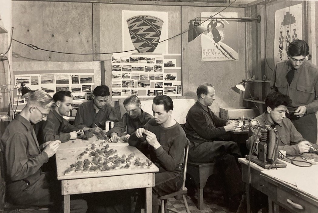 Men work around a table in a room with three posters on the wall