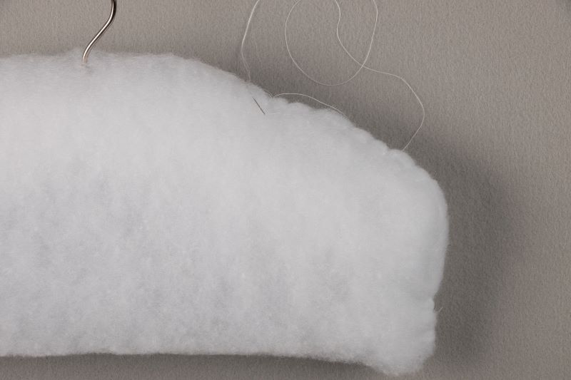 Demonstrating how to hand-stitch batting around the hanger.