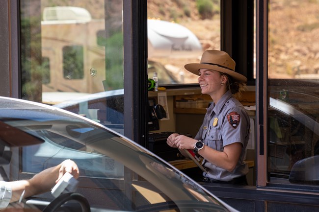 a smiling female park ranger greets a visitor at an entrance station