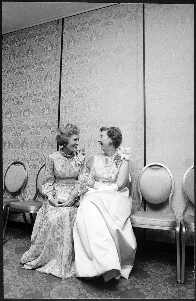 A black and white image showing Pat Nixon and Mamie Eisenhower seated and laughing together