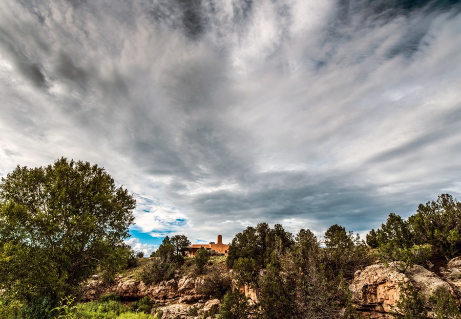 A blanket of white and gray clouds over a rocky, tree-covered hill with a pink house at the top.