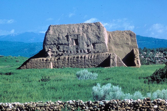 Mission church at Pecos NHP Old mission church mud walls in a grassland with tree covered mountains in the background.
