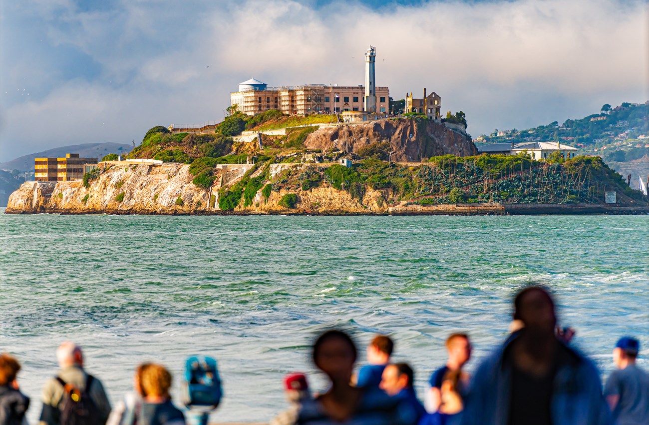 Alcatraz island, with blurry figures in the foreground and a blue, cloudy sky