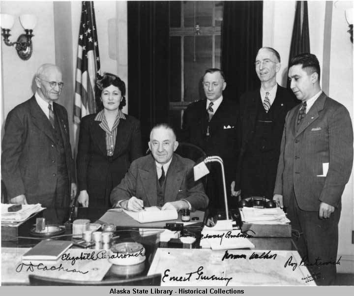 a woman and four men standing around a man at a desk