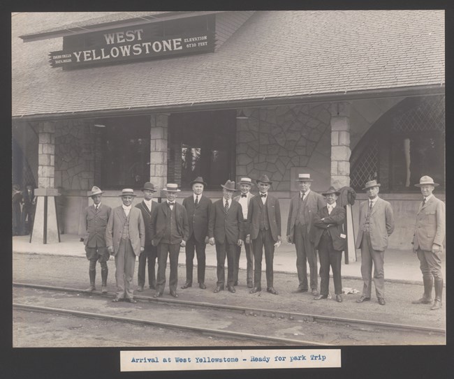 A dozen men stand on train tracks posing for a photo