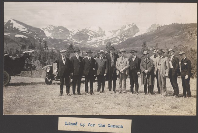 Twelve men stand in a line posing for the photograph with a mountain range behind
