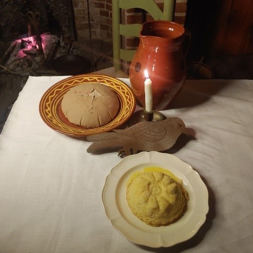 A small round pudding sits on a dish next to a candle, bread, and a pitcher.