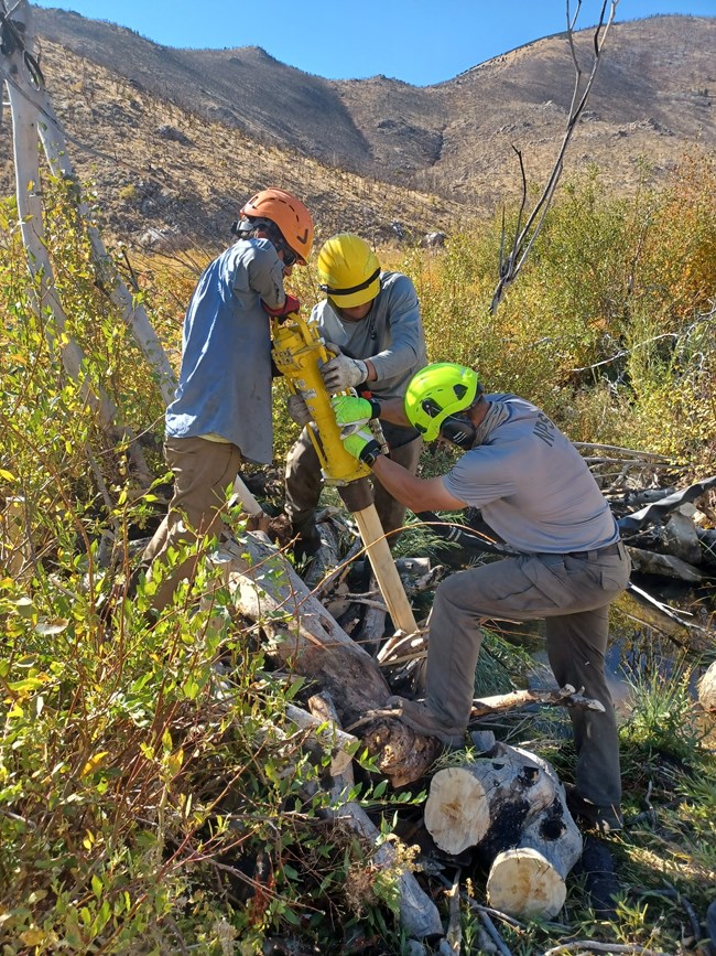 three people with helmets pounding on a stick