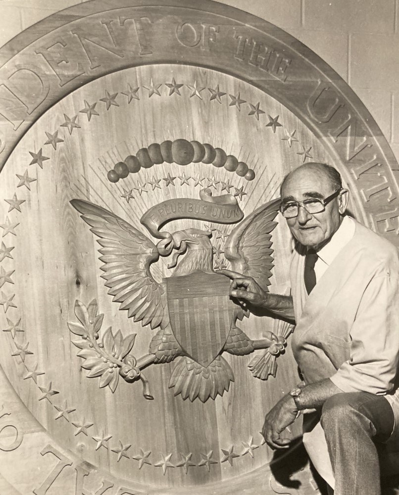 John Segeren poses next to a large round presidential seal he carved.