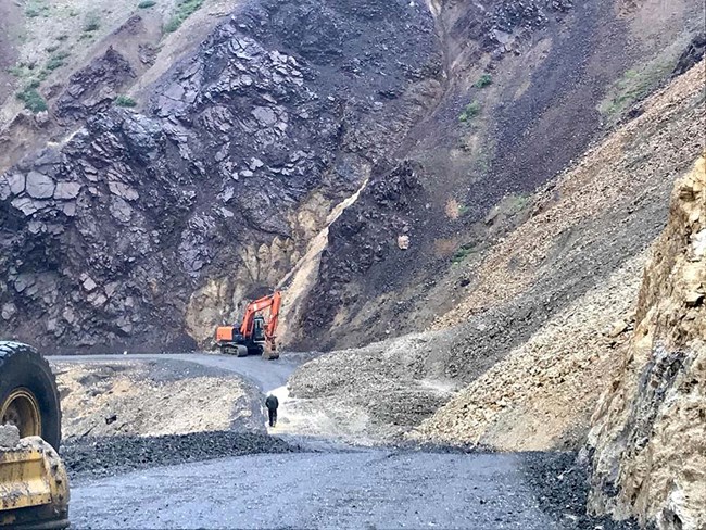 A large landslide is being cleared on a narrow gravel road.