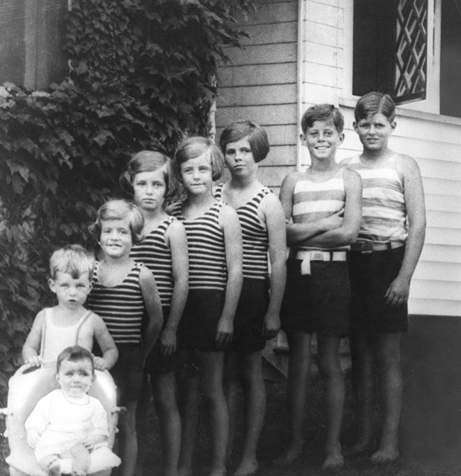 Black and white photo of eight Kennedy children in order of their age.  Joe Jr. is to the far right.