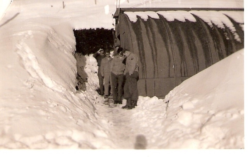 group of men in overcoats standing by Quontset hut and snow above their heads.