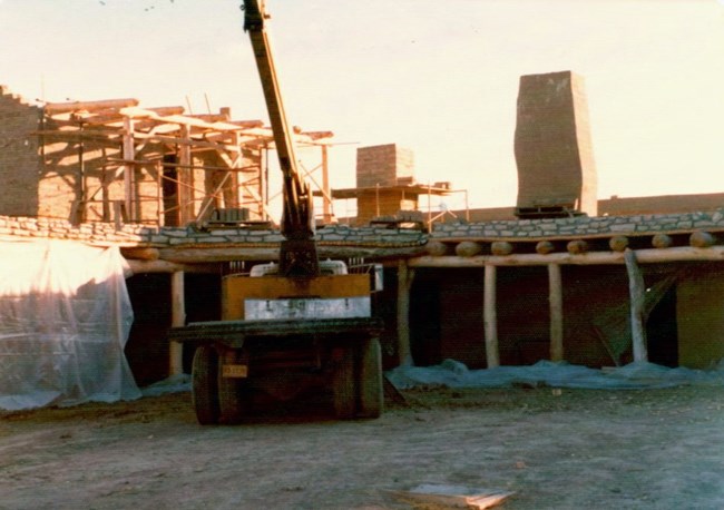 Construction of the reconsturction, 1975 A truck is next to an adobe walled structure under construction.