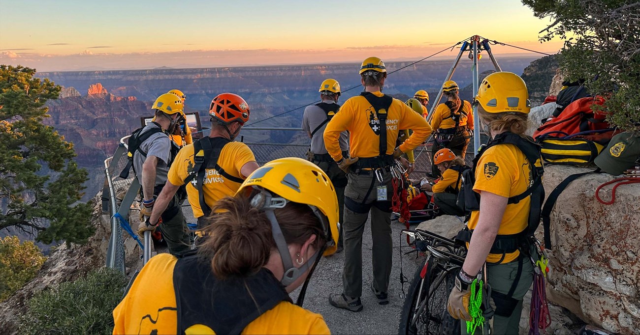 Ten search and rescue personnel wearing yellow shirts and helmets are performing a rescue at a scenic overlook with guard rails.