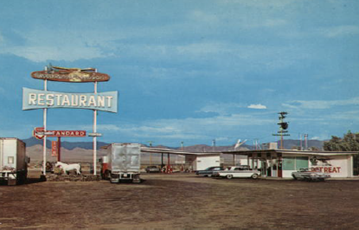 A large neon sign in front of a historic one-story motel.