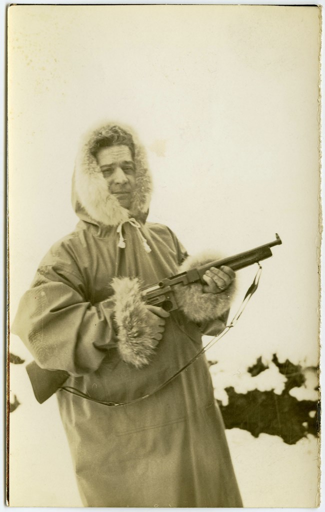 sephia toned photo of a man in heavy winter clothes holding a gun