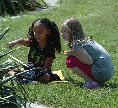 Art in the Park Two children sitting in the grass, one pointing to something in the distance.