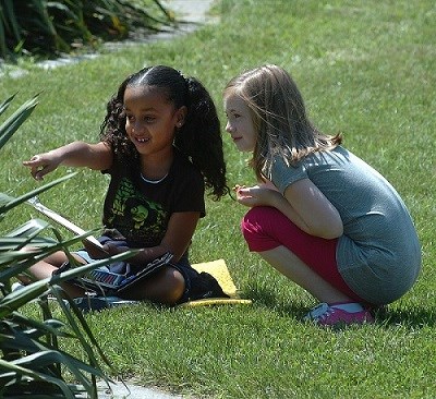 Two children sitting in the grass, one pointing to something in the distance.