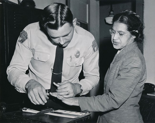 A man in police uniform fingerprinting a woman wearing glasses