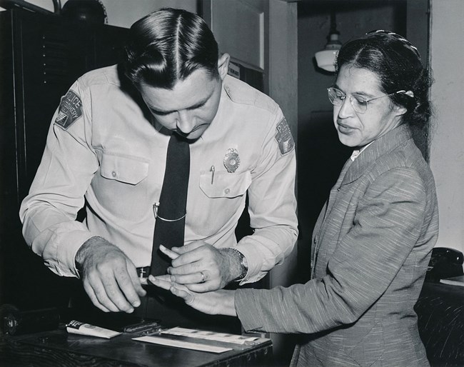 Rosa Parks being fingerprinted by Deputy Sheriff D.H. Lackey after being arrested on February 22, 1956, during the Montgomery bus boycott A man in police uniform fingerprinting a woman wearing glasses