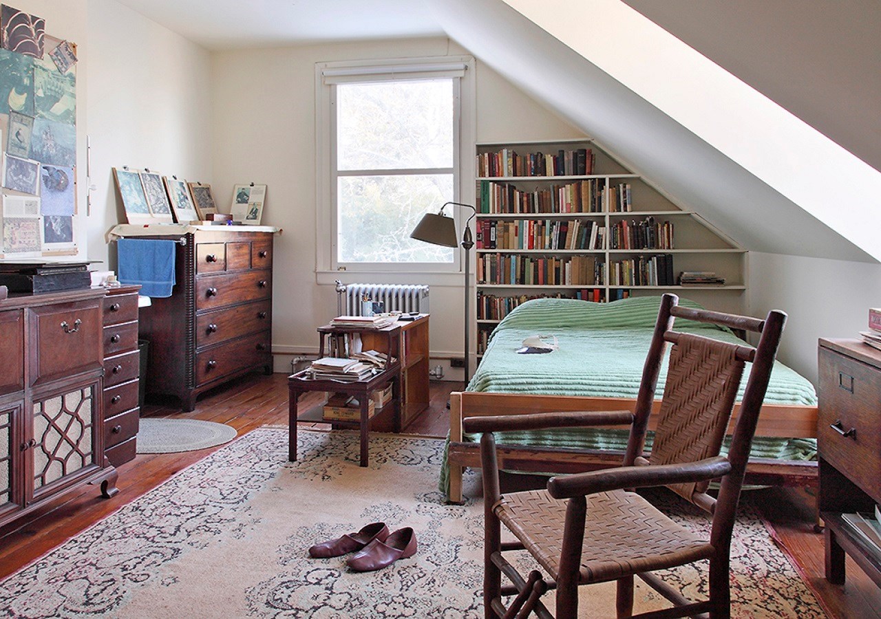 A loft bedroom with bed, two dressers, a wall bookshelf. Paper ephemera is on the desk and walls.