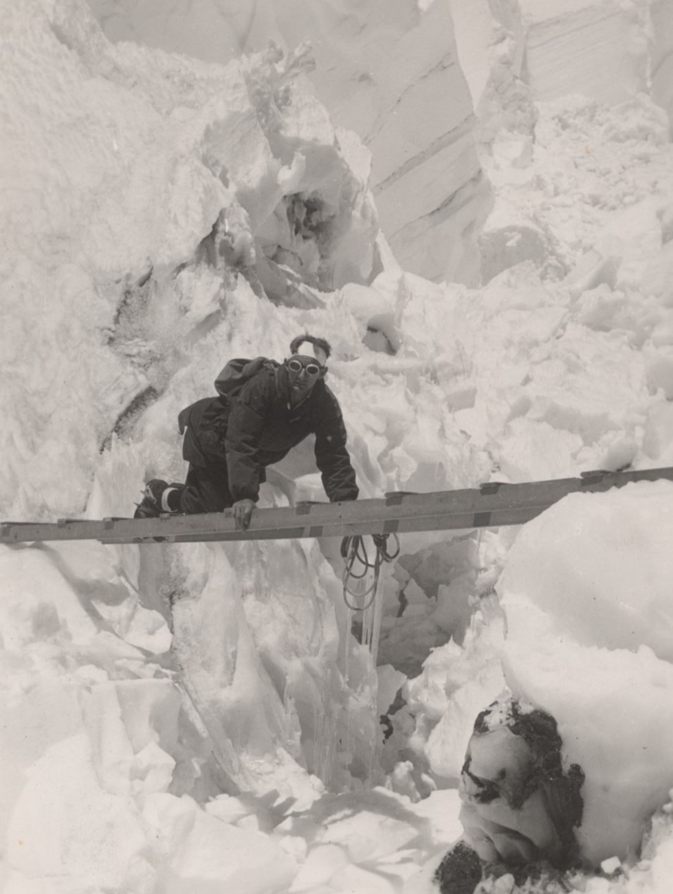 Man in climbing gear crawling across a ladder that spans a crevasse