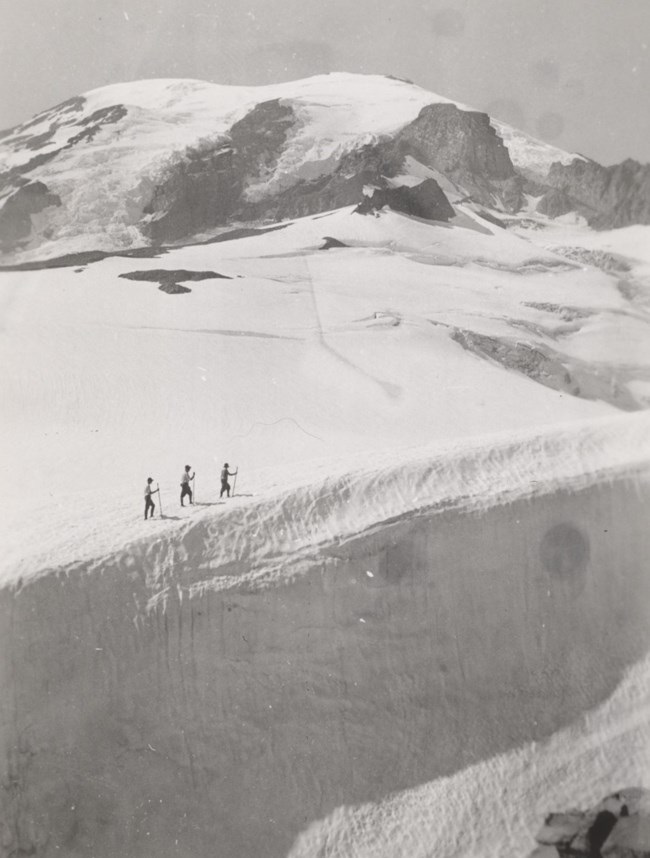 Three people seen in the distance walking along a glacier