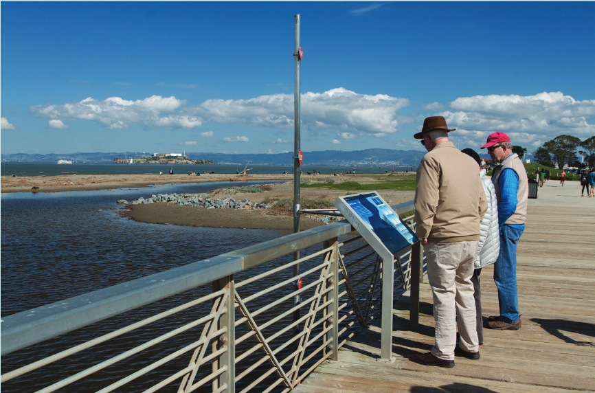 Visitors stop to check out a sign and sea level rise markers overlooking Crissy Marsh.