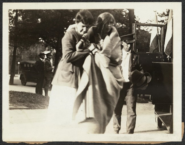 Suffragist Kate Heffelfinger being assisted as she leaves Occoquan workhouse. Photograph of a woman escorting Kate Heffelfinger, wrapped in blanket, outside near a car, after release from jail.