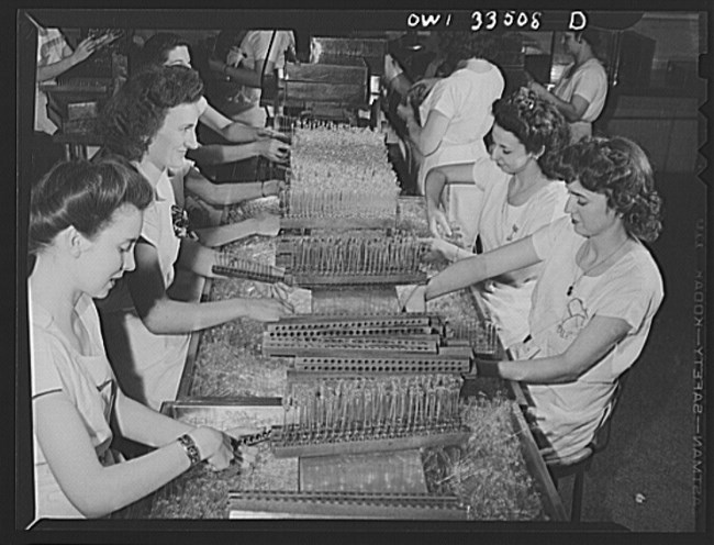 Women in mid 20th century working in factory handling glass tubes.