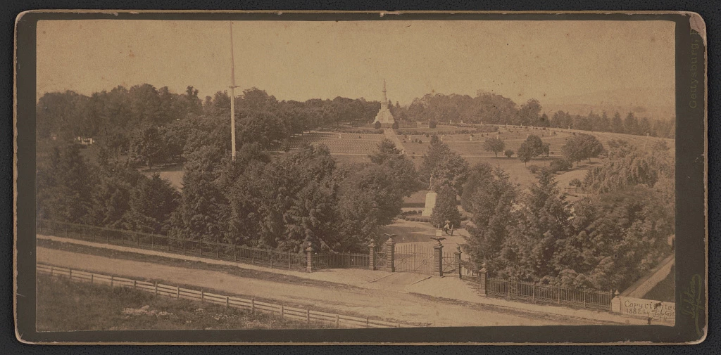 Soldiers National Cemetery at Gettysburg ca. 1882 Photograph shows gate to Gettysburg National Cemetery in front of statue of Major General John F. Reynolds with the Soldiers' National Monument in the distance, surrounded by grave markers.