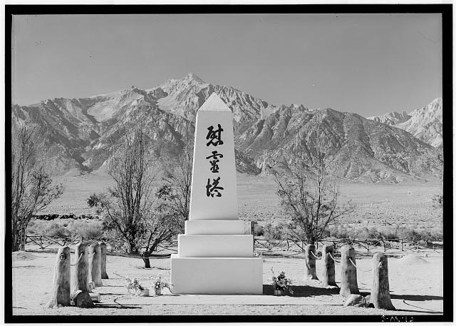 A white obelisk with three kanji characters stands in front of mountains in the California desert.