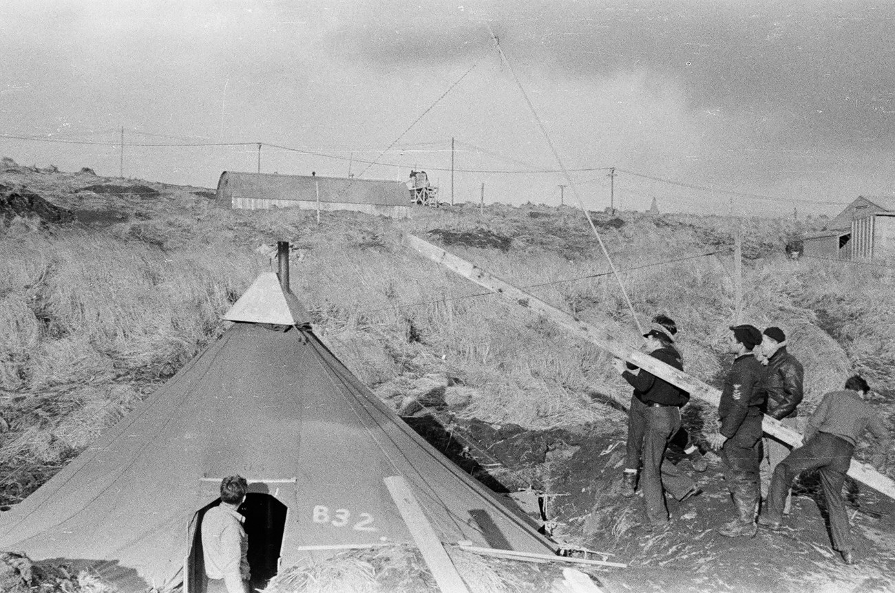 Servicemen at Work Black and white photo of men in uniform working on wing of airplane in a field.