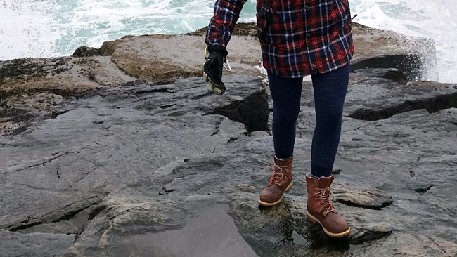 visitor steps across wet rocks close to crashing waves