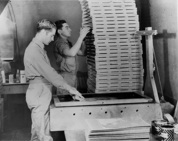 Two men standing at a silkscreen printing press