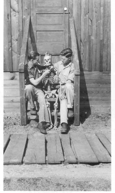 two young ccc members sit on a stoop with a skeleton, making it smoke a cigarette