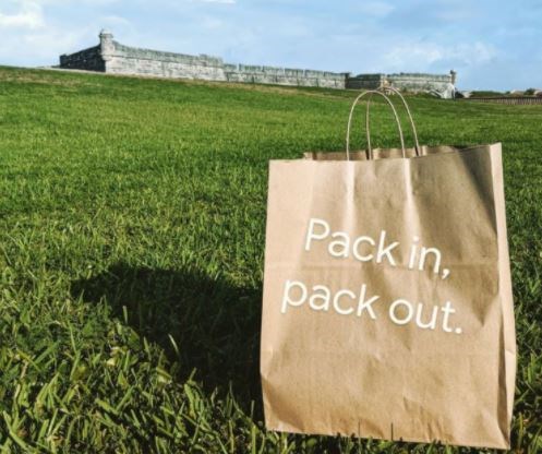 Image of a brown bag on fort lawn and it says, "Pack in, pack out."