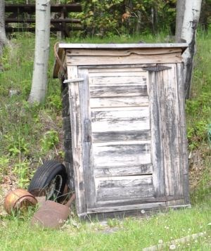 Historic small wood slat shack with junk leaning against it.