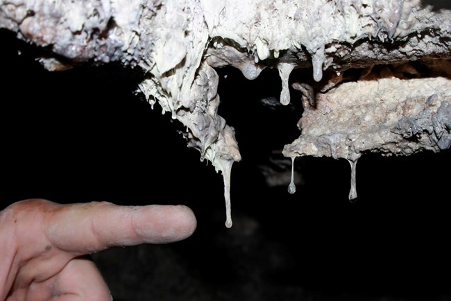 a finger points at a dripping white cave feature