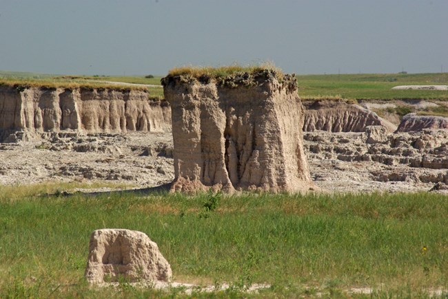 lt= an elevated portion of prairie stands over green grasses and in front of badlands canyons.