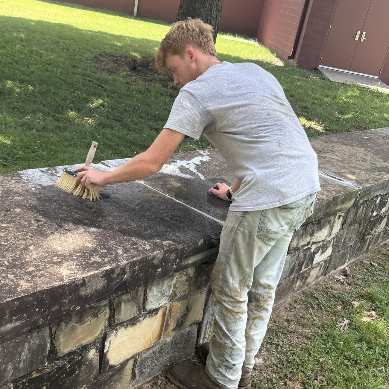 A person scrubs the top of a stone wall with a brush.