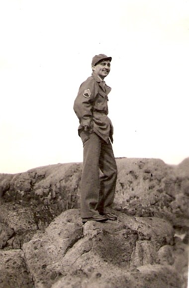 Smiling man in uniform standing on large rocks.