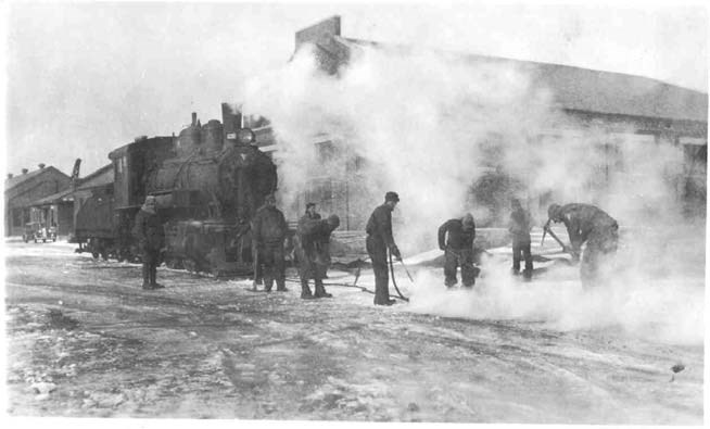 7 men stand in a cloud of steam coming off of a train engine