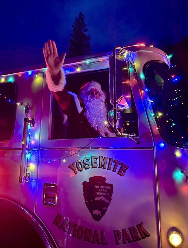 Steve Lyon A man dressed as Santa waves from a fire engine decorated with multi-colored lights.