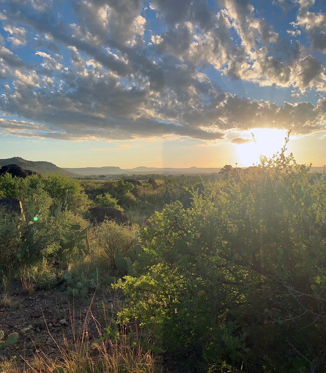 Fort Davis National Historic Site sun low on the horizon lighting up the clouds and desert shrubs and cactus.