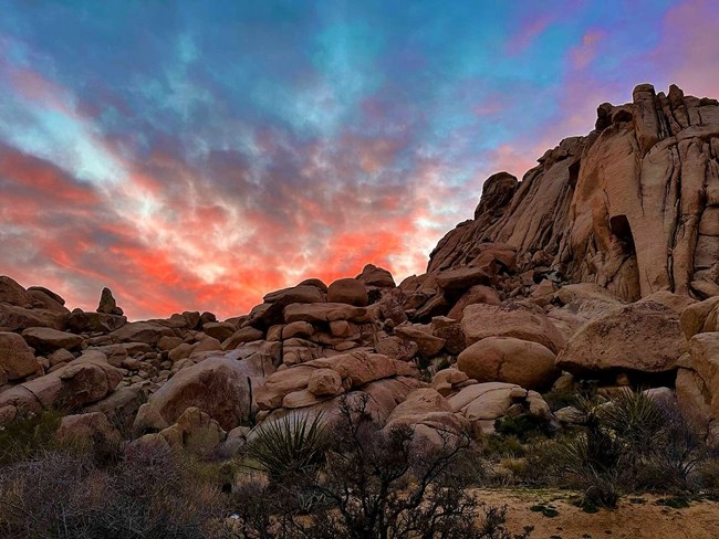 Sunset behind desert rock formations Light blue sky with brilliant orange clouds behind a rocky desert landscape.