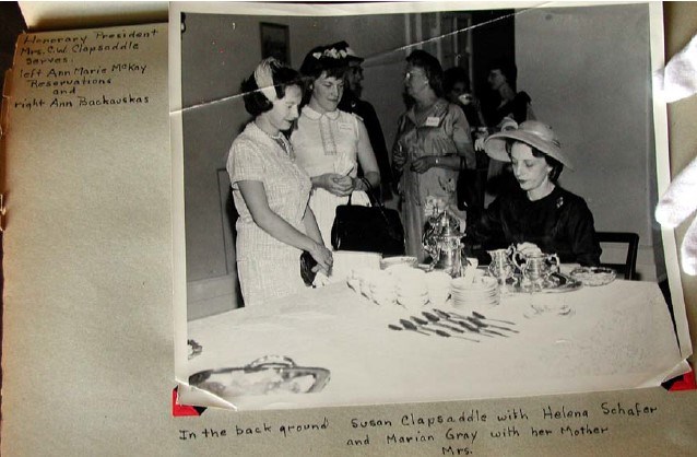 three women in fancy dress stand around a table