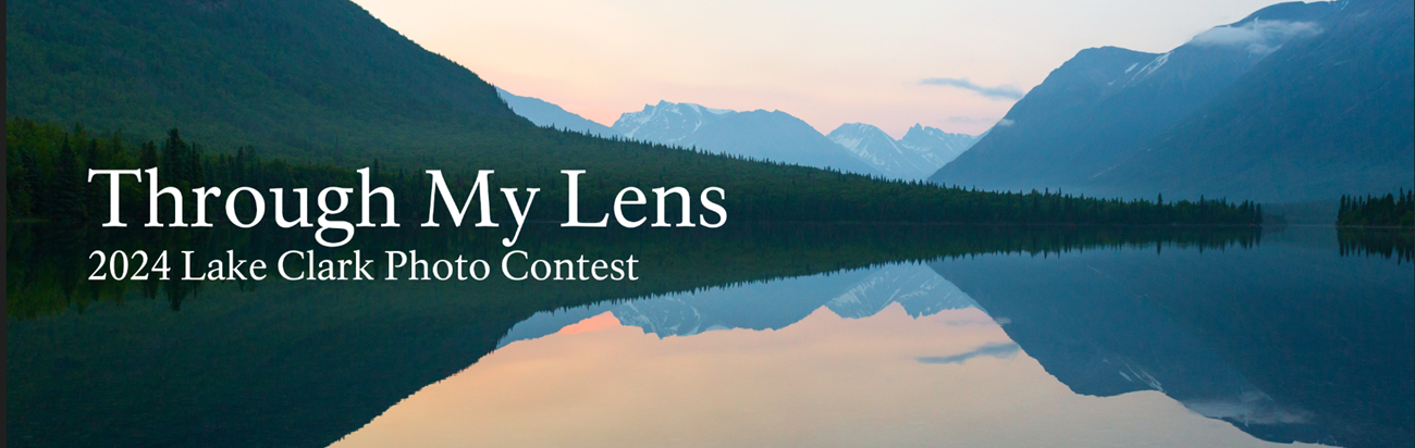 A lake reflects a sunset background with mountains and trees in the distance. To the center left is text saying "Through My Lens 2024 Lake Clark Photo Contest"
