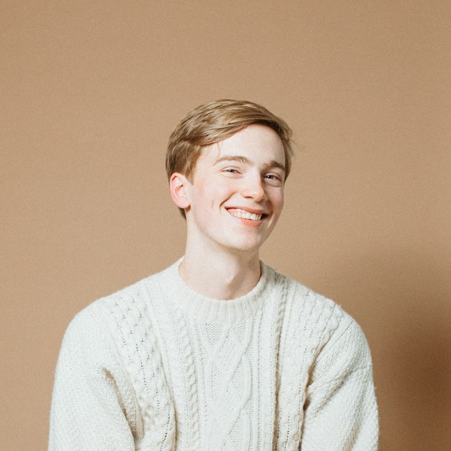 Smiling young man with strawberry blond hair wearing a white sweater